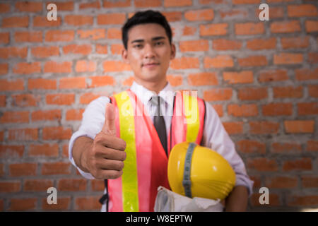Asian engineer man with blueprints showing thumbs up with brick wall background Stock Photo