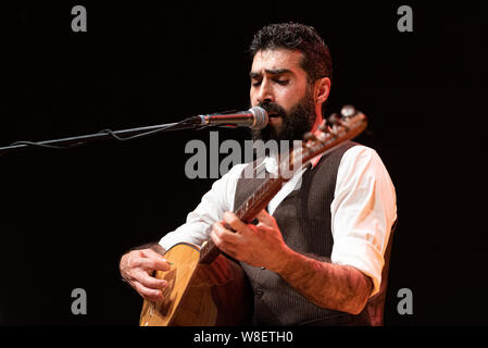 Good-looking man with a thick black beard, musician playing a typical stringed instrument on stage, the tembur or saz Stock Photo