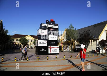 --FILE--Customers walk past logos of fashion brands at the Beijing Scitech Premium Outlet Mall in Beijing, China, 7 June 2014.   China has a shopping Stock Photo