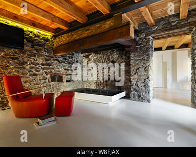 interior shots of a rustic living room with resin floor in the foreground the leather armchair and the rustic fireplace the walls are made of stone Stock Photo