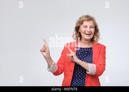 mature woman smiling broadly, pointing fingers away, showing something interesting and exciting Stock Photo