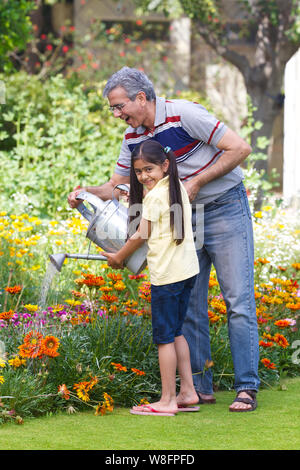 Old man watering plants with his granddaughter Stock Photo