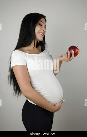 beautiful pregnant brunette woman holding fresh apple smiling standing half a turn on isolated white background Stock Photo