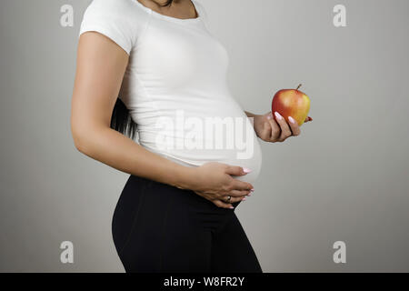 pregnant brunette woman holding red fresh red apple smiling standing half a turn on isolated white background Stock Photo