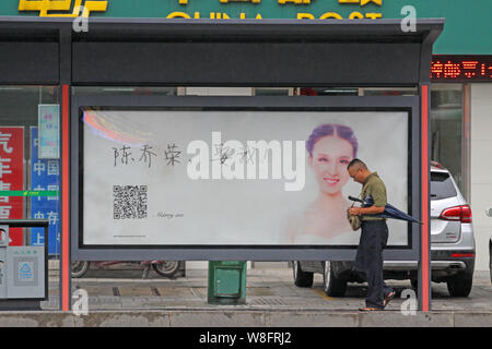 A pedestrian walks past an advertisement with a photo of a woman wearing her wedding dress and Chinese characters, which means 'Chen Qiaorong, Marry m Stock Photo