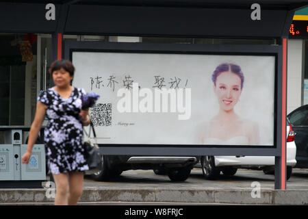 A pedestrian walks past an advertisement with a photo of a woman wearing her wedding dress and Chinese characters, which means 'Chen Qiaorong, Marry m Stock Photo