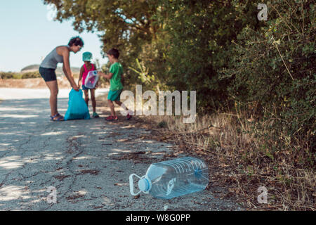 Young woman teaching her children to be environmentally responsible while picking up trash in the countryside Stock Photo