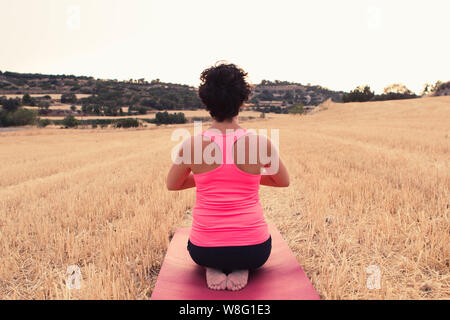 Young girl doing yoga in the middle of a wheat field. Meditation and relaxation concept. Stock Photo