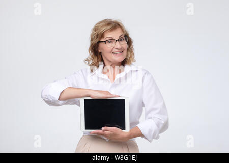 Mature caucasian woman shows a screen digital tablet. Stock Photo