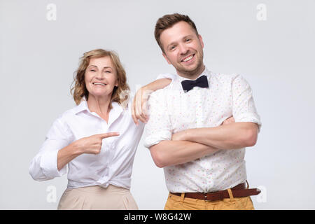 Mature woman boss pointing on young male coworker praising him. Stock Photo