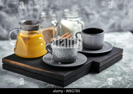 Transparent glass teapot with chitrus tea and cups, tea set on a wooden table. Close up, gray background, soft light. Stock Photo