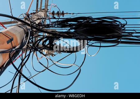 Electric pole with many and disordly cables. Opposite view of an electric pole with blue sky in background. Stock Photo