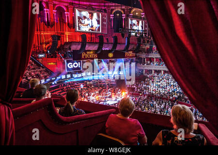 The Royal Albert Hall Audience BBC Proms performance interior viewed from luxury plush private box in auditorium with sound & spectacular light effects & dramatic eclectic music performance by 'Public Service Broadcasting' and The Multi-Story Orchestra, of a work entitled 'The Race For Space' an audio visual spectacular honouring mans achievements in space. Proms Promenade Concerts Royal Albert Hall Kensington London UK Stock Photo