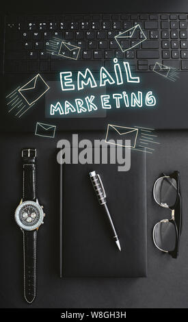 A laptop, watch, pen, notebook and glasses lying on a black desk. Hand drawn doodle illustration on the shot. Vertical flat-lay Stock Photo