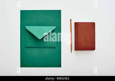 Isolated kraft paper sheet and envelope on a white background next to a notebook and a pencil. Horizontal flat-lay Stock Photo