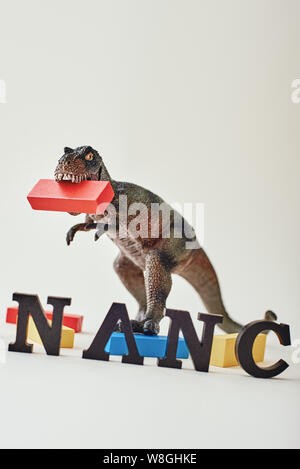 Close up of red, blue and yellow wooden blocks placed unevenly over light background near dinosaur toy. Word Finance made of wooden letters standing in a row. Vertical shot Stock Photo
