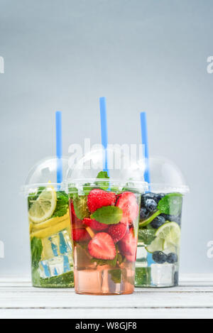 Various lemonade with fruits and berries in a plastic cups with drink straws on blue background. Take away drinks concept. Stock Photo