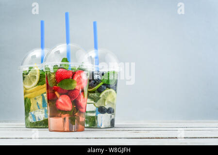 Various lemonade with fruits and  berries in a plastic cups with drink straws on blue background. Take away drinks concept. Stock Photo