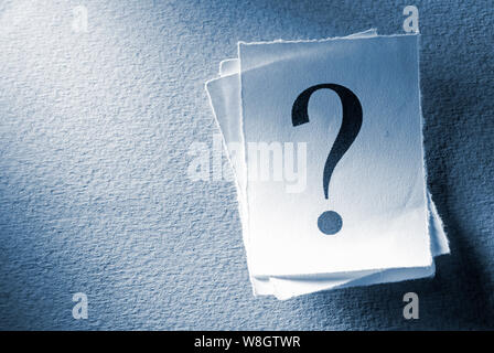 Pile of printed question marks in shaft of light on a textured grey background with copy space in a conceptual image Stock Photo