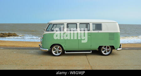 Classic Green and white  VW Camper Van parked on Seafront Promenade. beach and sea in the background Stock Photo