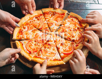 Hands taking pizza slices from wooden table, close up view. Stock Photo