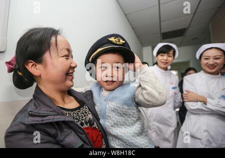 The four-year-old legless boy Xiao Feng, second left, puts on the hat of a pilot of China Eastern Airlines as he is carried by his mother at Zhongnan Stock Photo