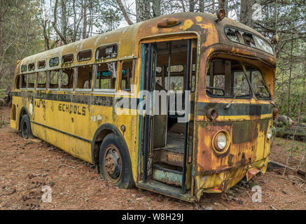 Old rusting abandoned school bus in a junkyard with blue sky in winter ...