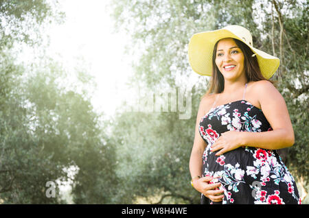 Pregnant Peruvian woman in a forest, beautiful young Peruvian girl waiting for a child, a naughty woman with dark hair in dress with hat on nature Stock Photo