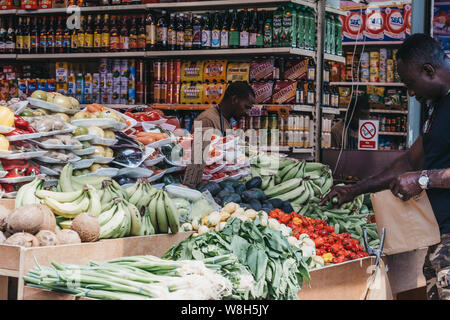 London, UK - July 16, 2019: Man buys fresh fruits and vegetables from a market stall at Brixton Market, a community market run by local traders in the Stock Photo