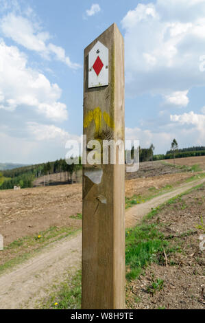 A wooden signpost  is standing next to a hiking trail through the hills in the Ardennes, Belgium. It is a sunny day with a blue sky and white clouds. Stock Photo