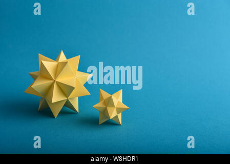 Two handmade yellow paper polyhedrons on a blue background. Stock Photo