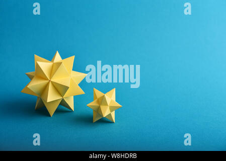 Two handmade yellow paper polyhedrons on a blue background. Stock Photo