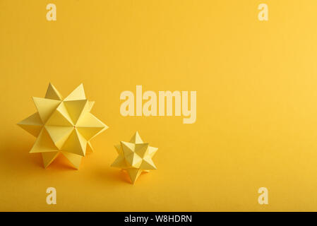 Two handmade yellow paper polyhedrons on a yellow background. Stock Photo
