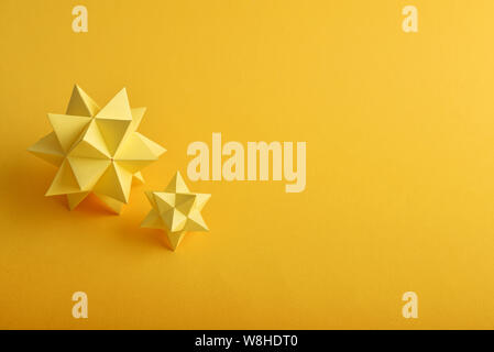 Two handmade yellow paper polyhedrons on a yellow background. Stock Photo
