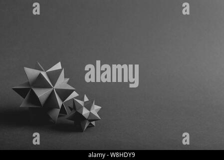 Two handmade grey paper polyhedrons on a grey background. Stock Photo