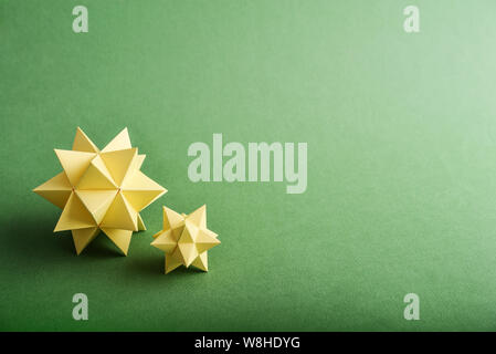 Two handmade yellow paper polyhedrons on a green background. Stock Photo