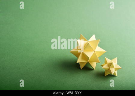 Two handmade yellow paper polyhedrons on a green background. Stock Photo