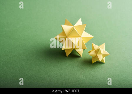 Two handmade yellow paper polyhedrons on a green background. Stock Photo