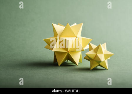 Two handmade yellow paper polyhedrons on a green background. Stock Photo