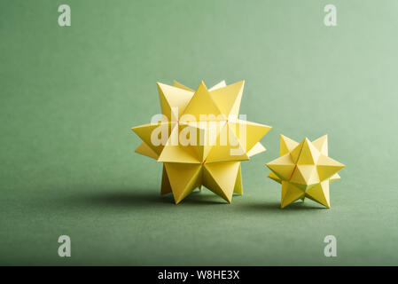 Two handmade yellow paper polyhedrons on a green background. Stock Photo