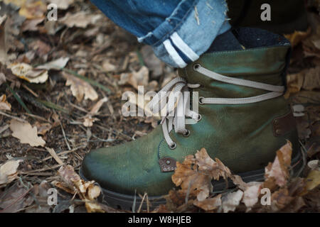 Close up of a leg in green hiking boots with laces in the autumn forest against a background of yellow fallen foliage, selective focus Stock Photo