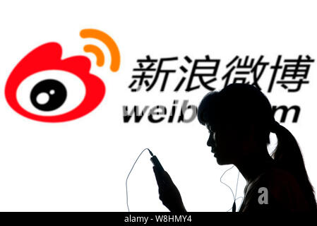 --FILE--A woman uses her mobile phone in front of a logo of weibo.com, the Twitter-like online microblogging service of Sina, in Shaoyang city, centra Stock Photo