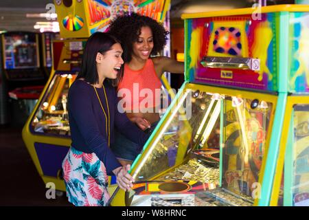 Two young women playing arcade game at fun fair. Stock Photo