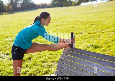 Young woman stretching leg on park bench. Stock Photo