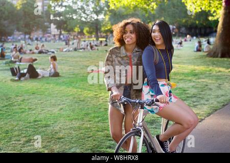 Two young women in park, one sitting on bicycle. Stock Photo