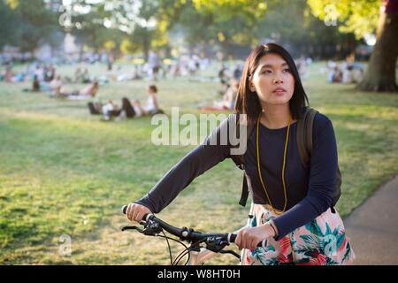 Young woman pushing bicycle in park. Stock Photo