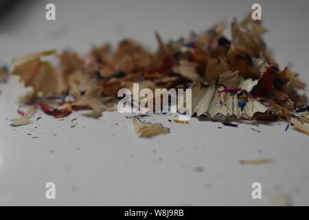 Multi-colored pencil shavings on a white/grey background with natural light shining through. Stock Photo