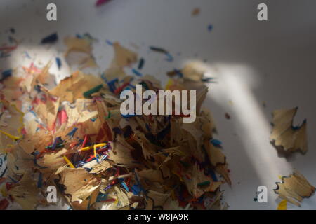 Multi-colored pencil shavings on a white/grey background with natural light shining through. Stock Photo