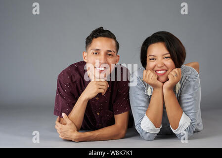 Smiling latin young couple lying isolated on gray studio background Stock Photo