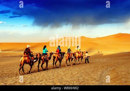 Tourists ride camels along the Mingsha Mountain (Singing Sands Mountain) of the Gobi desert in Dunhuang city, northwest China's Gansu province, 16 Jul Stock Photo